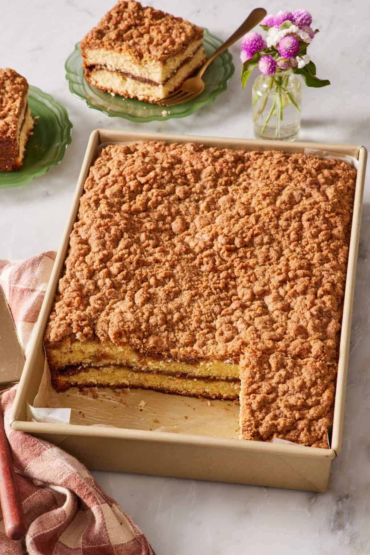 Coffee cake baked in a 9x13-inch pan with a few slices cut out and served on small plates in the background.