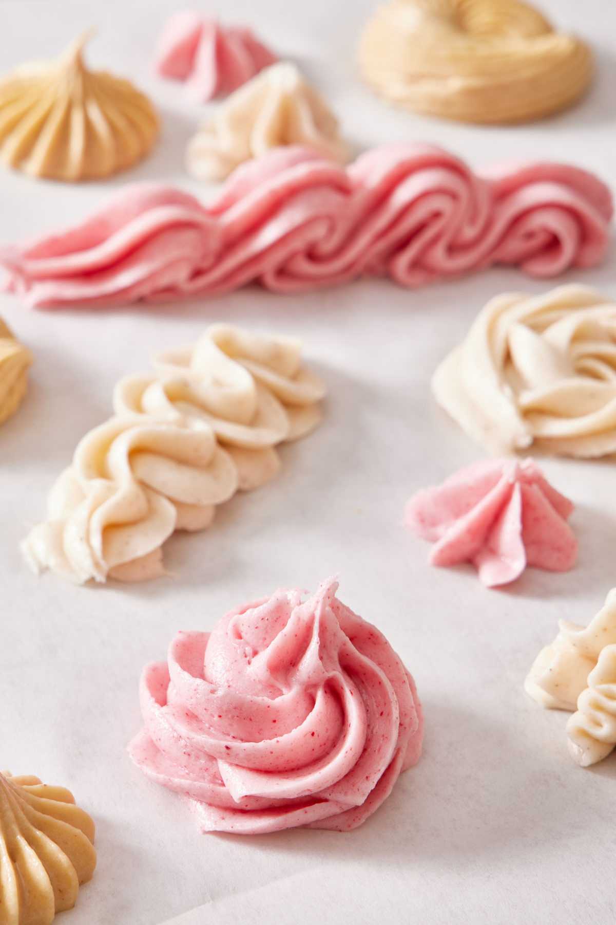 Flavor variations of cream cheese frosting piped in different patterns on a piece of parchment paper.