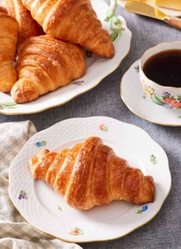 A homemade croissant on a plate with more croissants off to the side.
