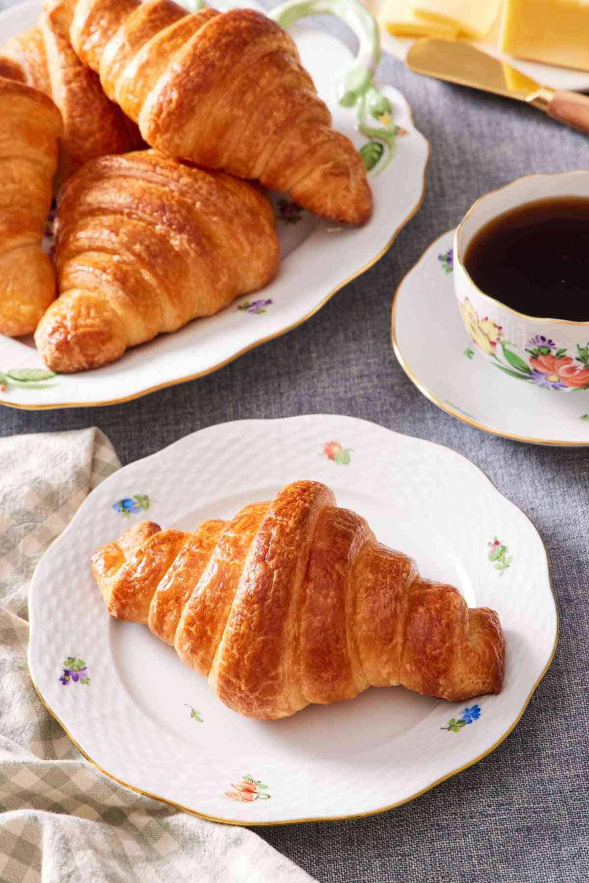 A homemade croissant on a plate with more croissants off to the side.