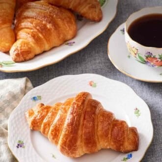 Pinterest graphic showing a croissant on a plate with coffee, with more butter croissants to the side.