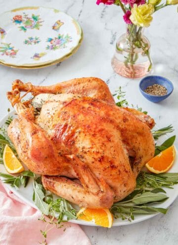 A roasted turkey on a bed of herbs and citrus on a platter.