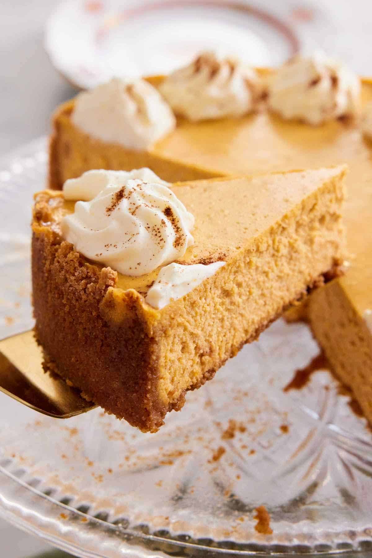 Close-up of a slice of pumpkin cheesecake lifted off a cake stand.