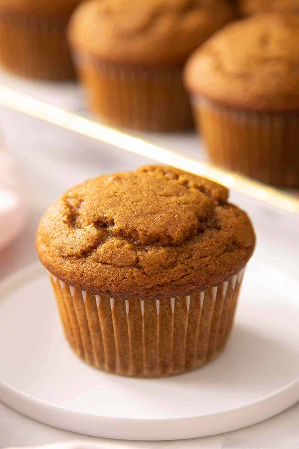 A pumpkin muffin on a small plate with more muffins out of focus in the background.