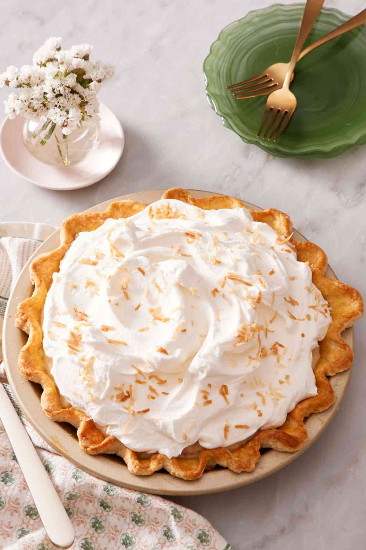 Coconut cream pie with serving plater and a small vase of flowers.