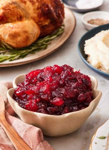 Close-up of a serving bowl of easy cranberry sauce with a turkey and mashed potatoes out of focus in the background.