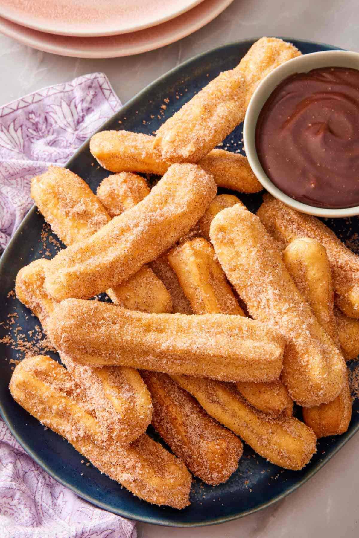 A platter of air fryer churros with a small bowl of chocolate sauce for dipping.
