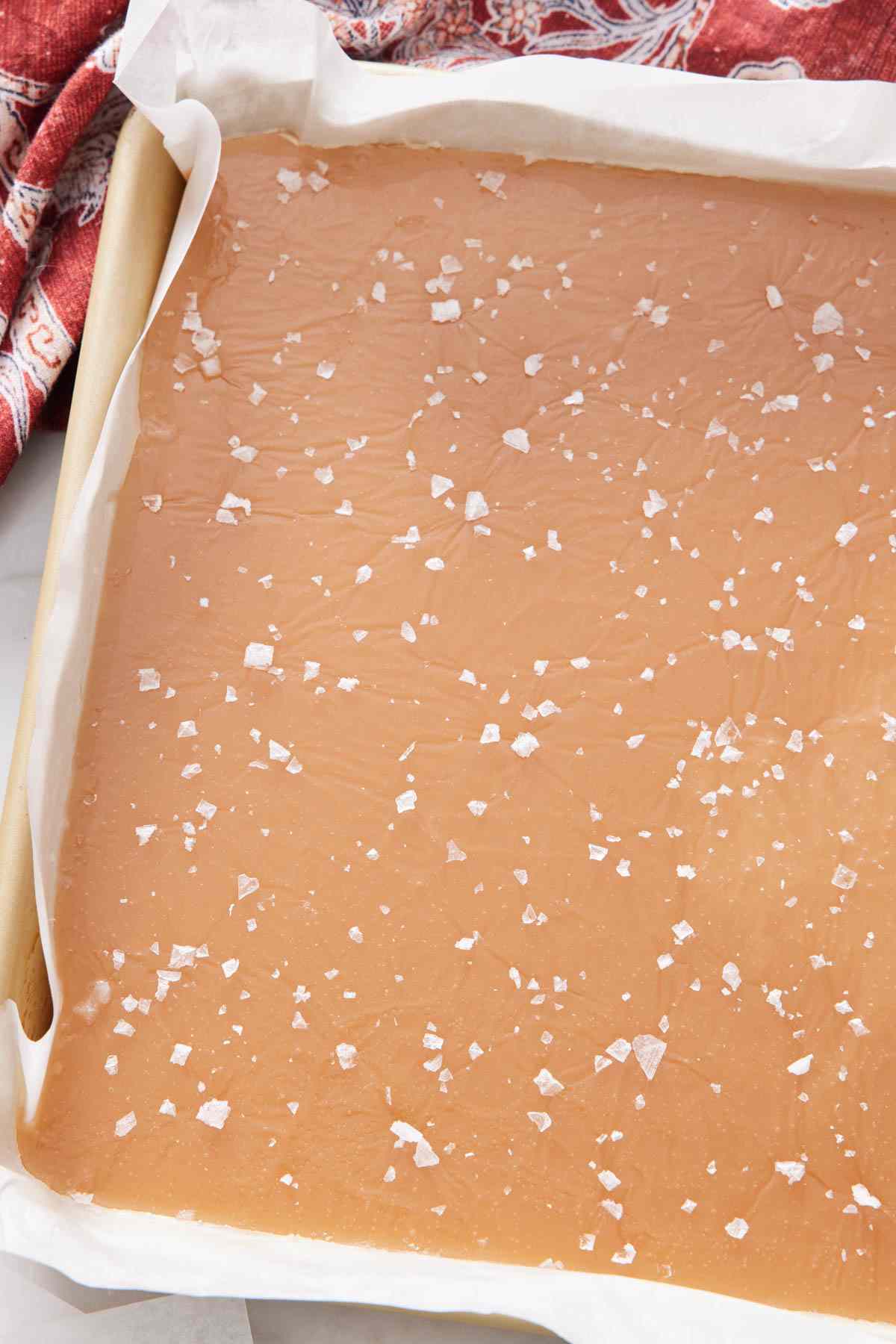 A baking sheet containing a slab of caramel sprinkled with flaky sea salt.