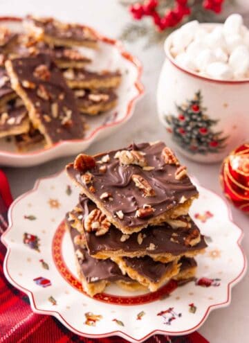 A stack of Christmas cracker candy on a plate with a mug of hot cocoa and more candy in the background.