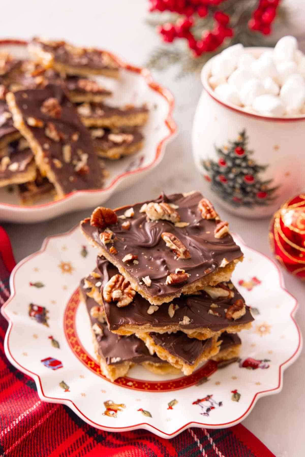A stack of Christmas cracker candy on a plate with a mug of hot cocoa and more candy in the background.