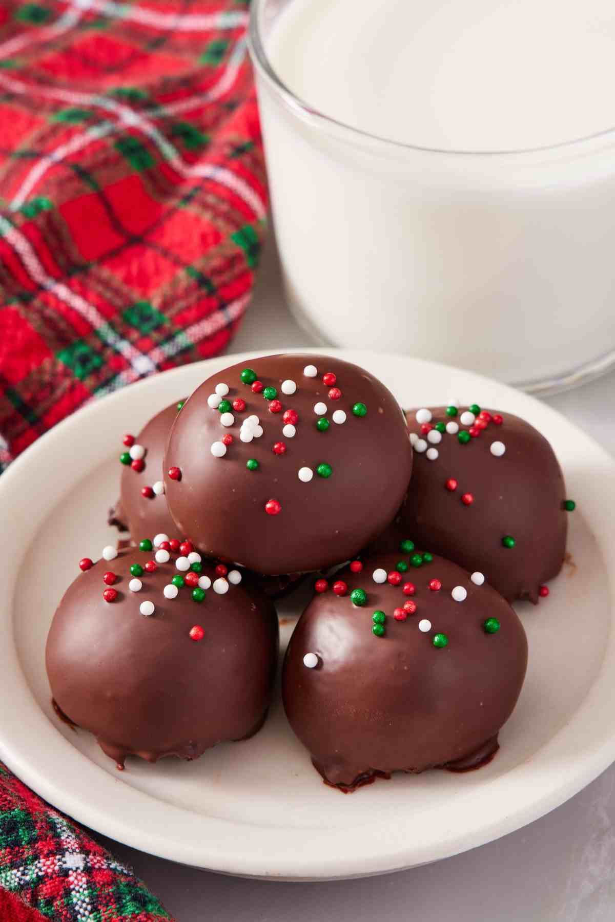 Five Oreo balls with festive sprinkles. A glass of milk and Christmas-themed linen in the background.