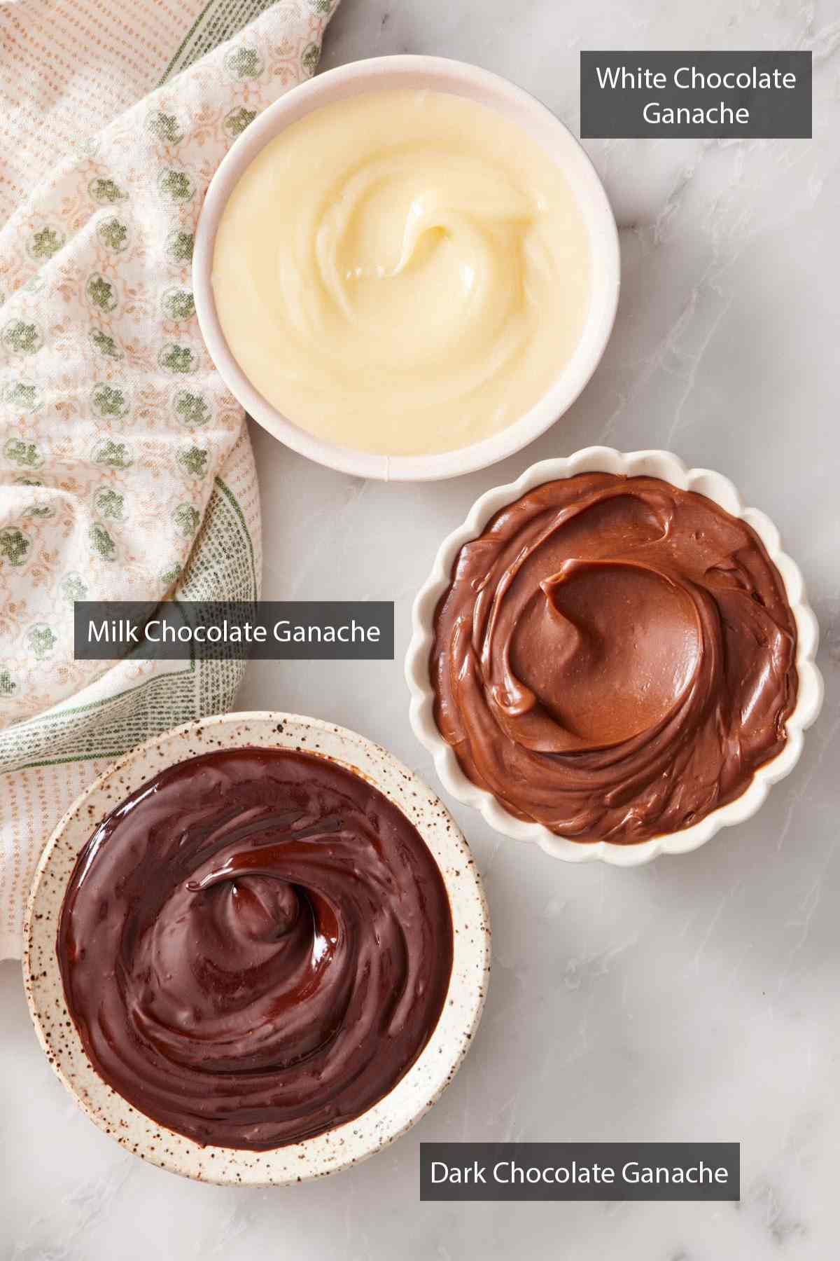 Overhead shot of three bowls of different types of chocolate ganache: milk chocolate, white chocolate, and dark chocolate.