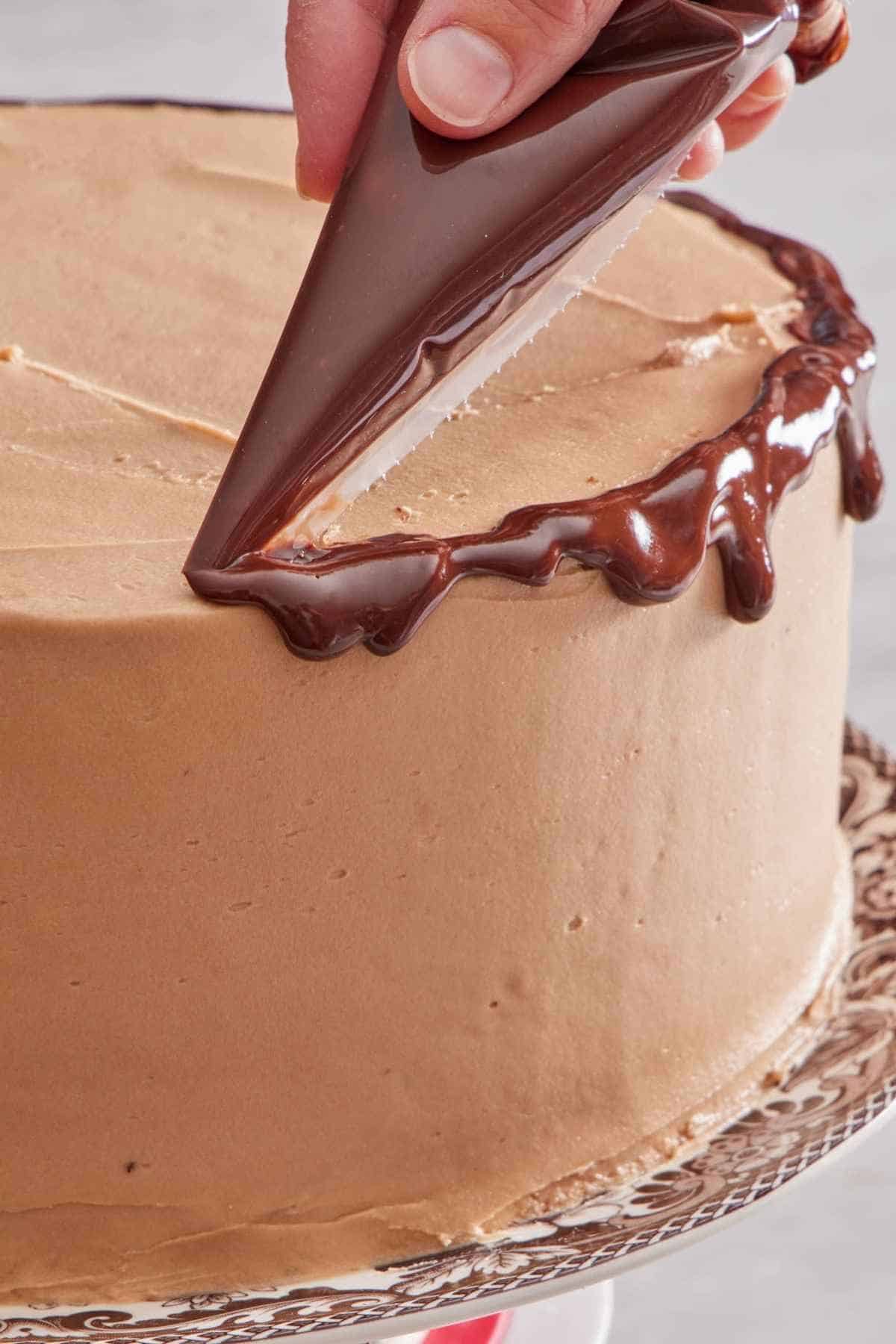 Close-up of a cake with a ganache drip being applied.