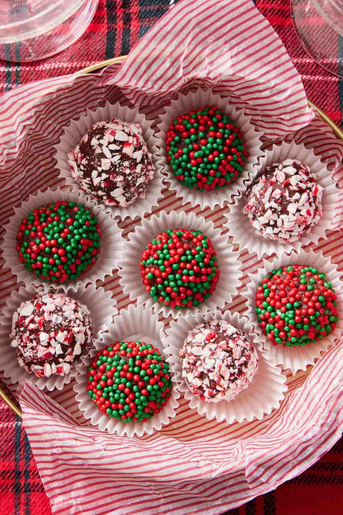 Several homemade chocolate truffles, some coated in red and green sprinkles, and some coated in crushed candy canes.