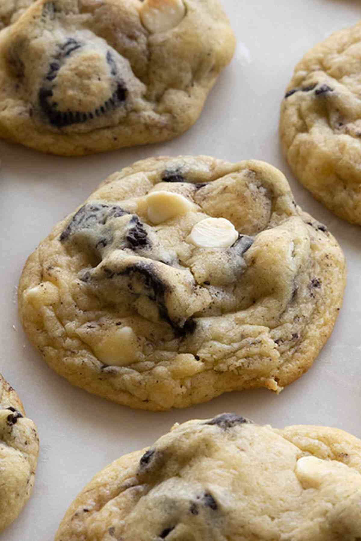 Close-up of a cookies and cream cookie on a marble surface, with more cookies partially in frame around it.