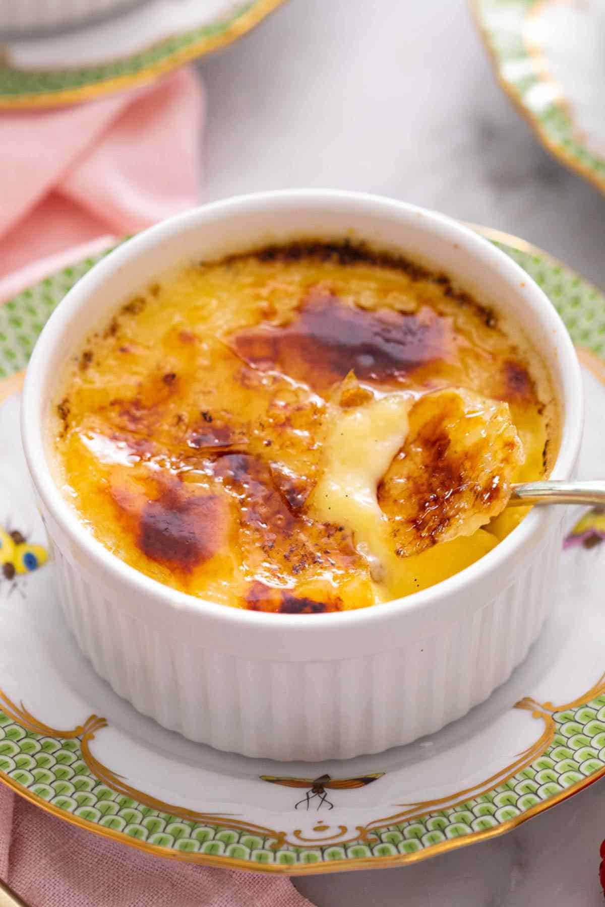 Crème Brûlée in a ramekin with a spoon inserted to showcase the crackly top and smooth custard.