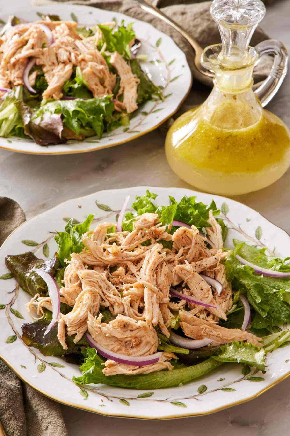 Instant Pot shredded chicken with red onions on a bed of greens with a container of salad dressing behind it.