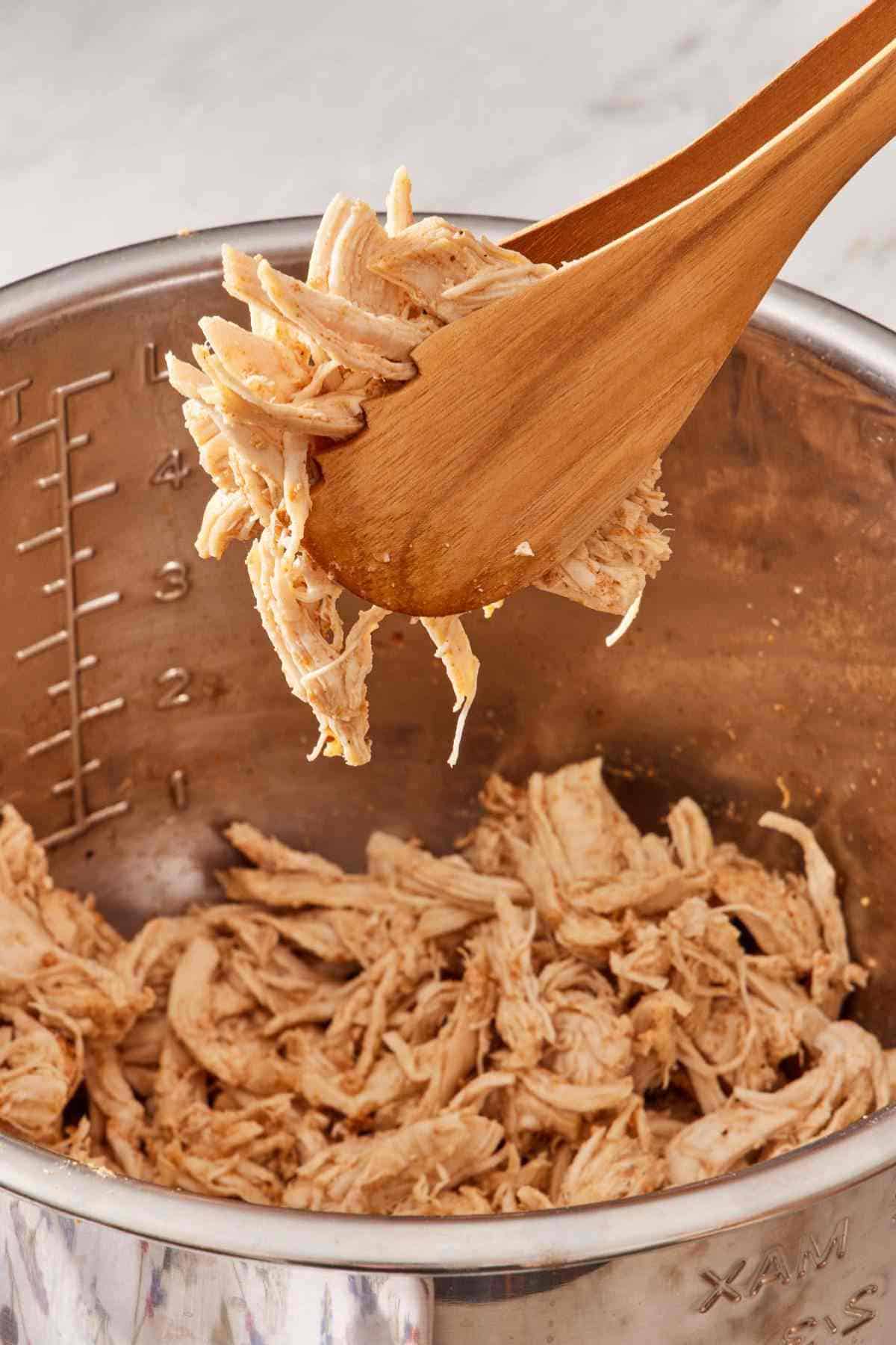 Instant Pot shredded chicken picked up out of the pot with wooden tongs.