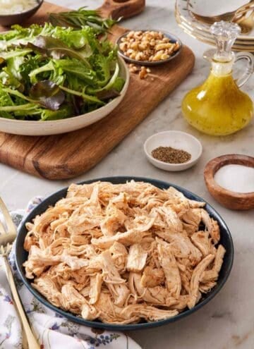A bowl of Instant Pot shredded chicken with salad greens and dressing in the background.