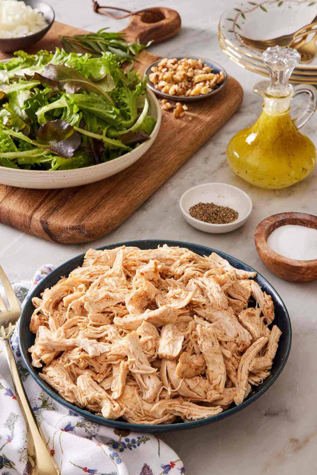 A bowl of Instant Pot shredded chicken with salad greens and dressing in the background.