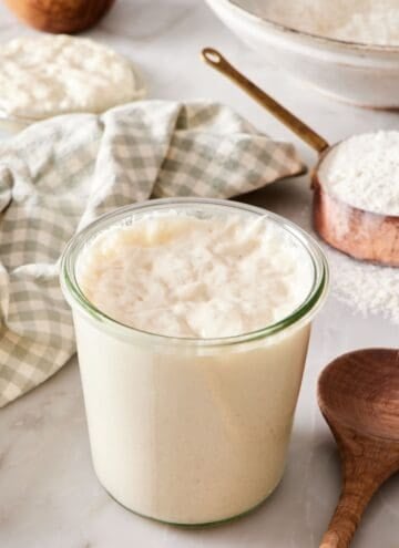 A jar of sourdough starter with a wooden spoon next to it.