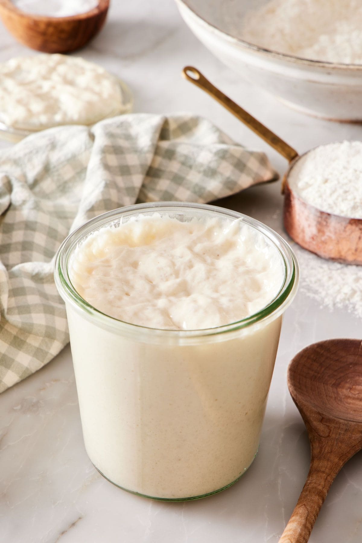 A jar of sourdough starter with a wooden spoon next to it.