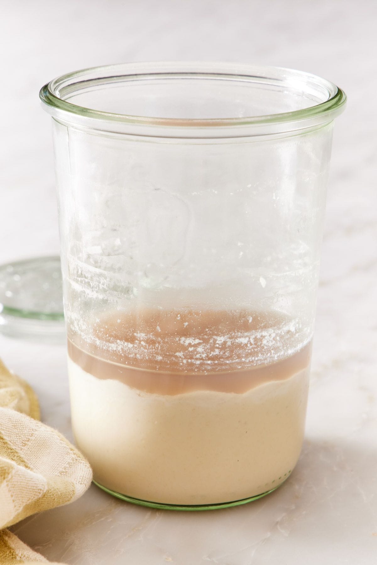 Sourdough starter in a glass jar with a layer of hooch formed on top of it.