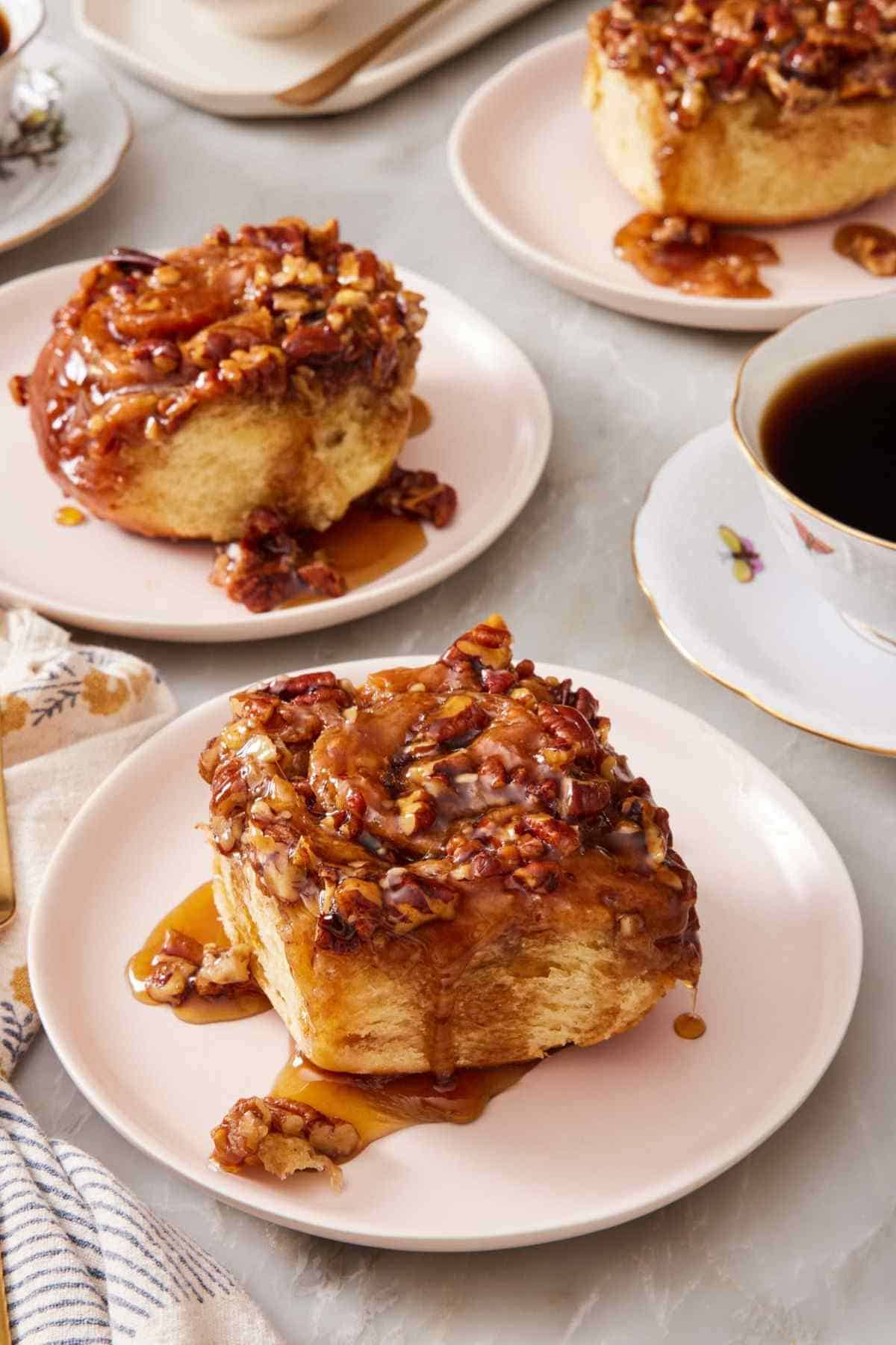 Sticky buns on separate small plates with a cup of coffee on the side.