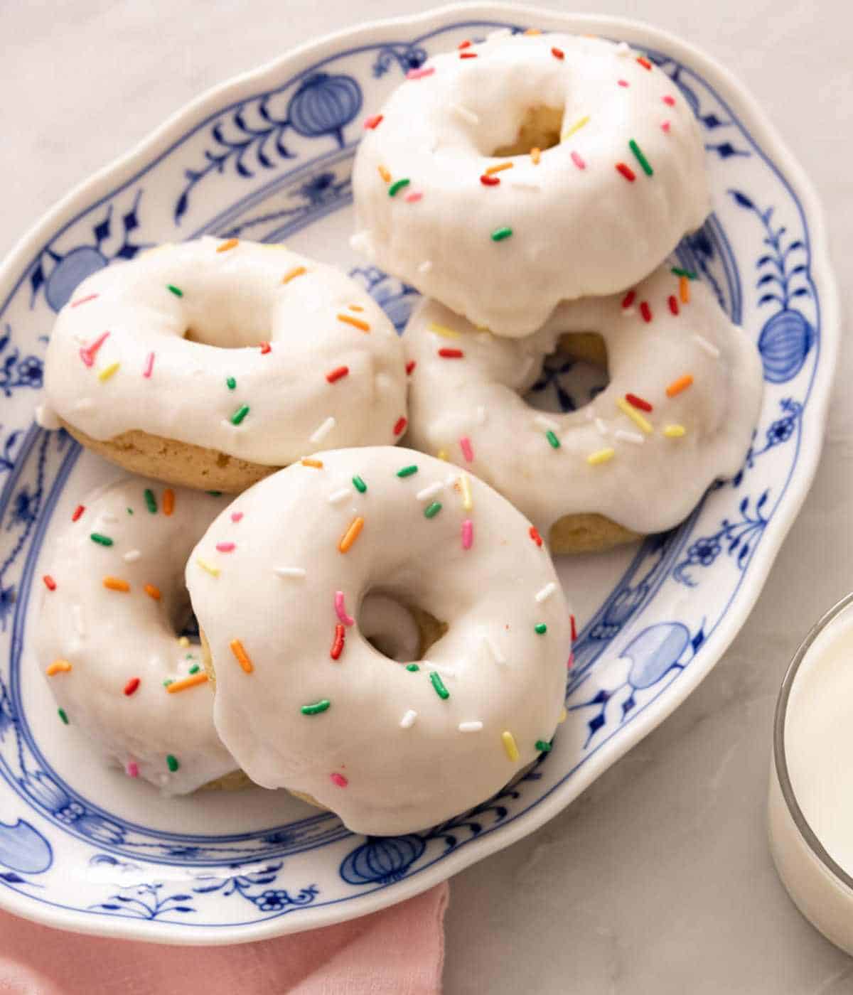 A batch of baked donut recipe topped with vanilla glaze on a blue and white platter.