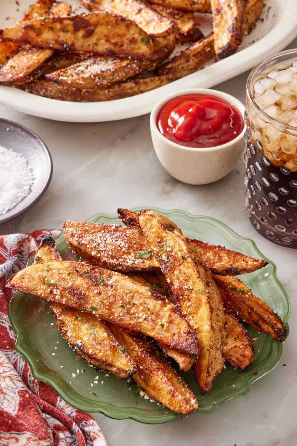 Baked potato wedges on a small plate with ketchup and a drink behind them.