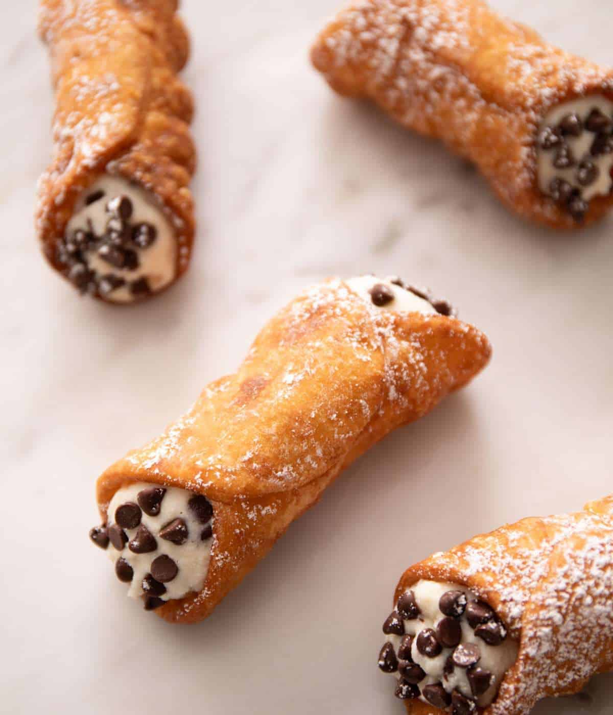 Cannoli with chocolate chips pressed into each end, placed on a marble countertop.
