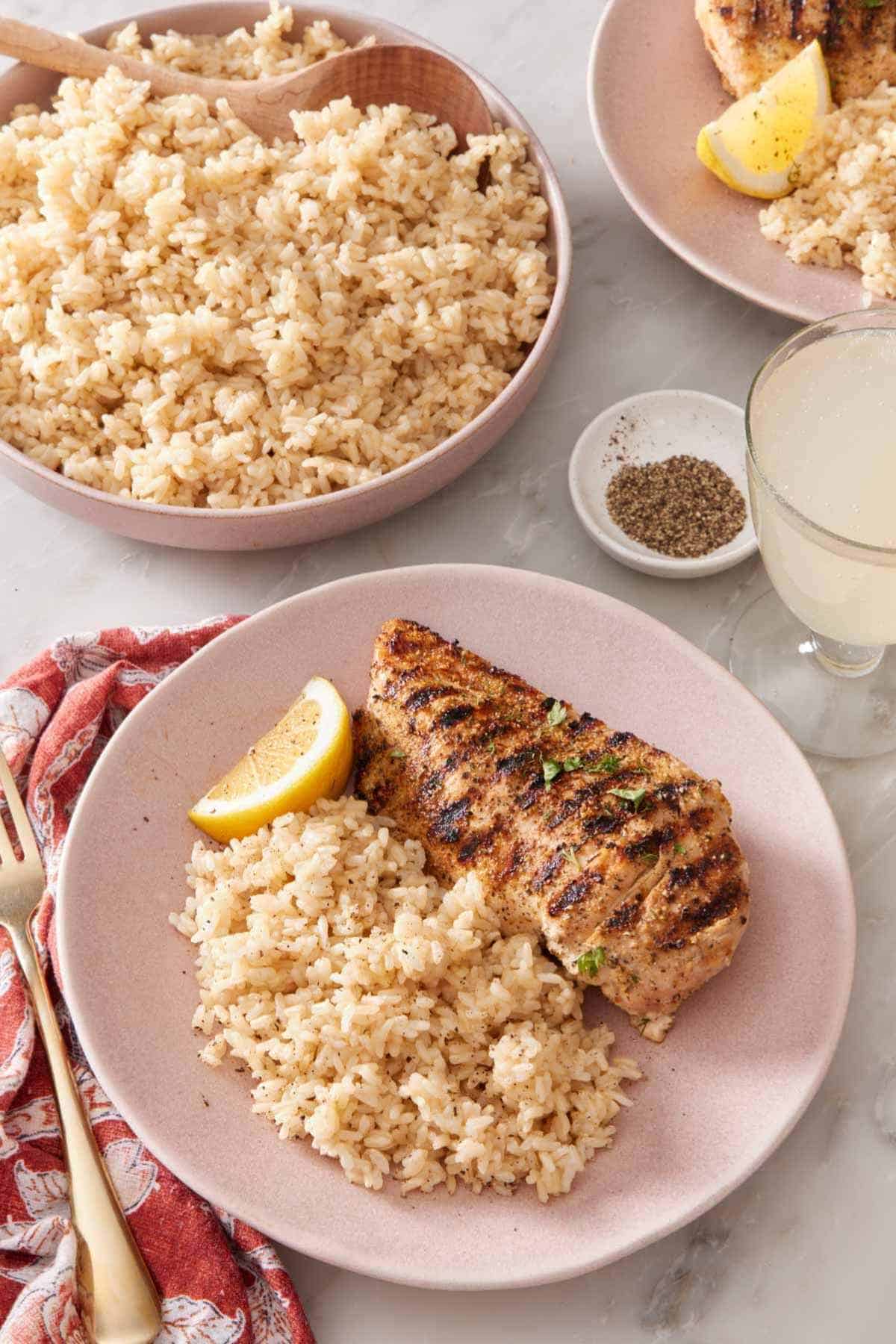 Grilled chicken with Instant Pot brown rice on a plate, with more rice in a serving bowl behind it.
