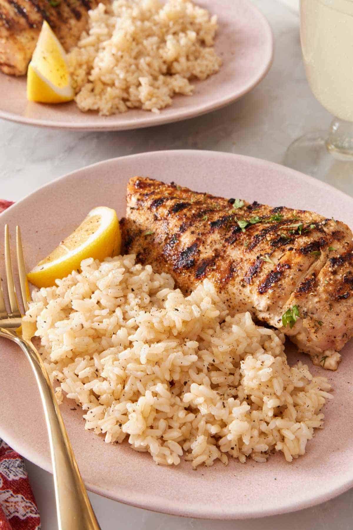 A chicken breast with brown rice and a lemon wedge on a plate.