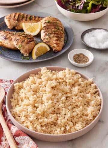 Serving bowl with Instant Pot brown rice, with grilled chicken breasts and salad greens in the background.