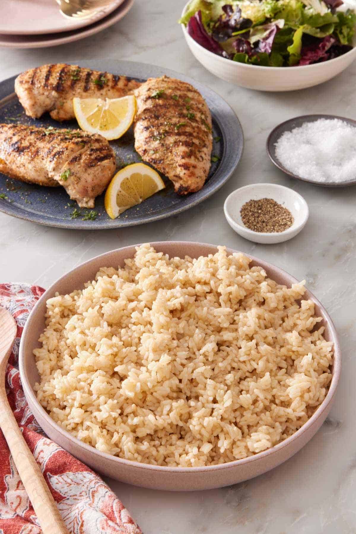 Serving bowl with Instant Pot brown rice, with grilled chicken breasts and salad greens in the background.