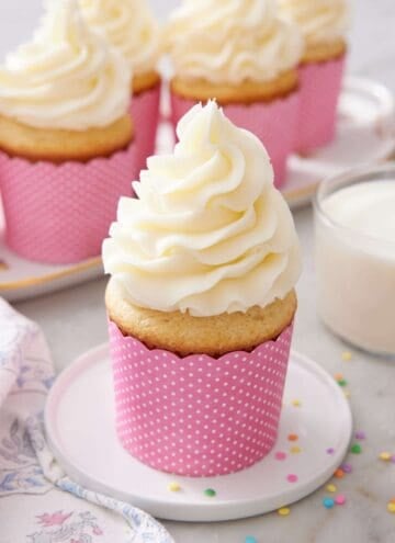 A frosted moist vanilla cupcake on a small plate.