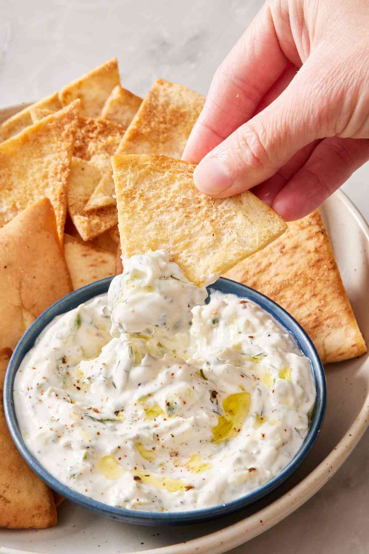 Homemade pita chip dipped into and lifted out of a bowl of tzatziki.