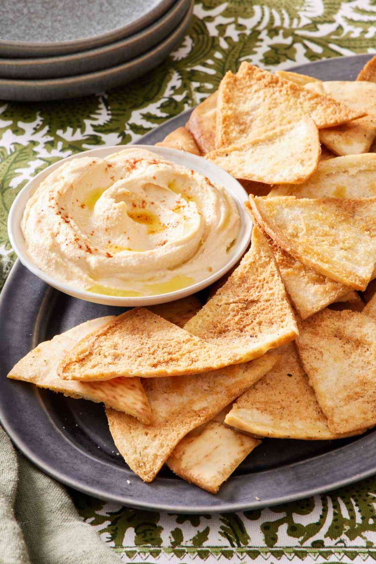 A platter of pita chips with a small bowl of hummus.