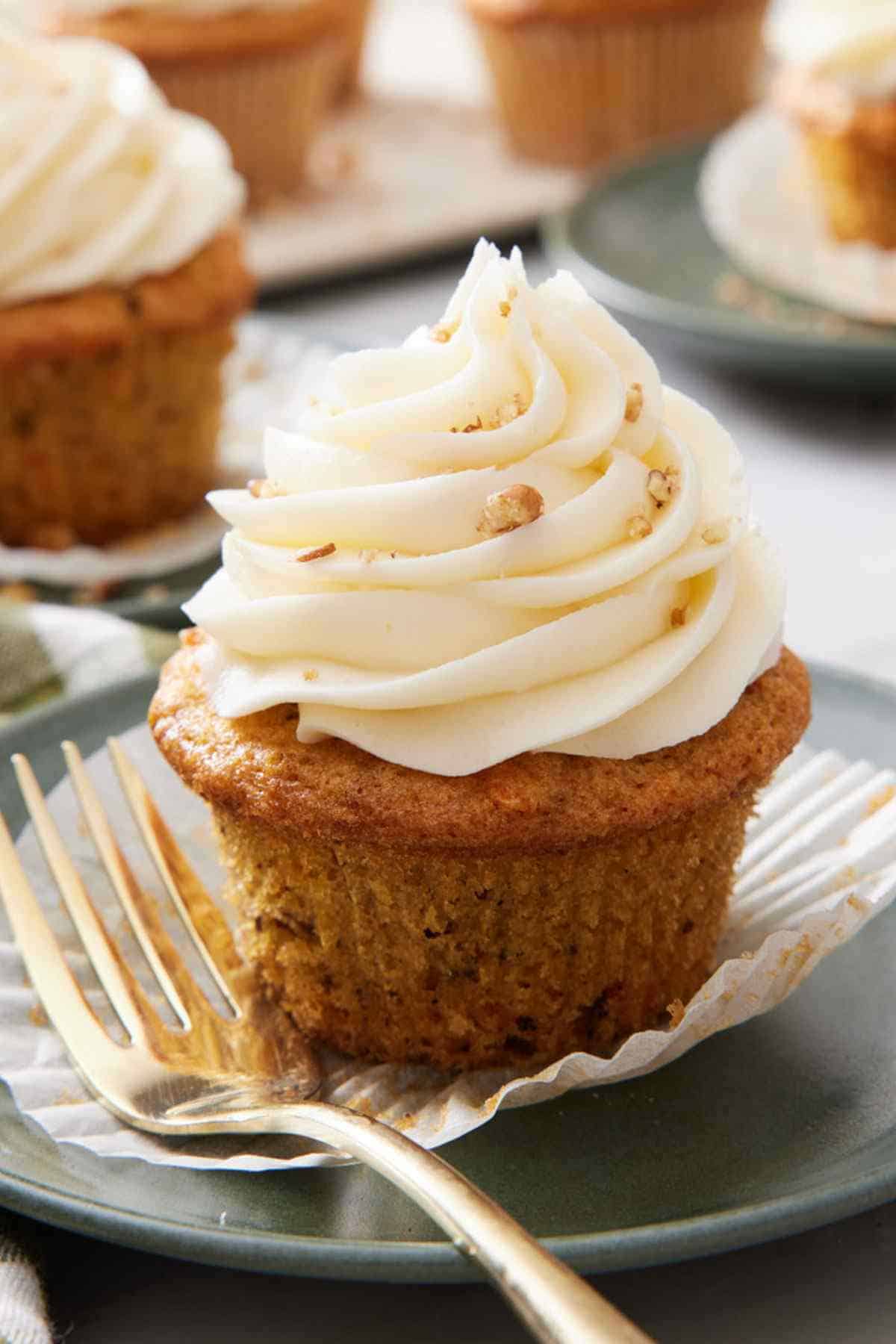 A carrot cake cupcake on a small plate with a fork next to it.