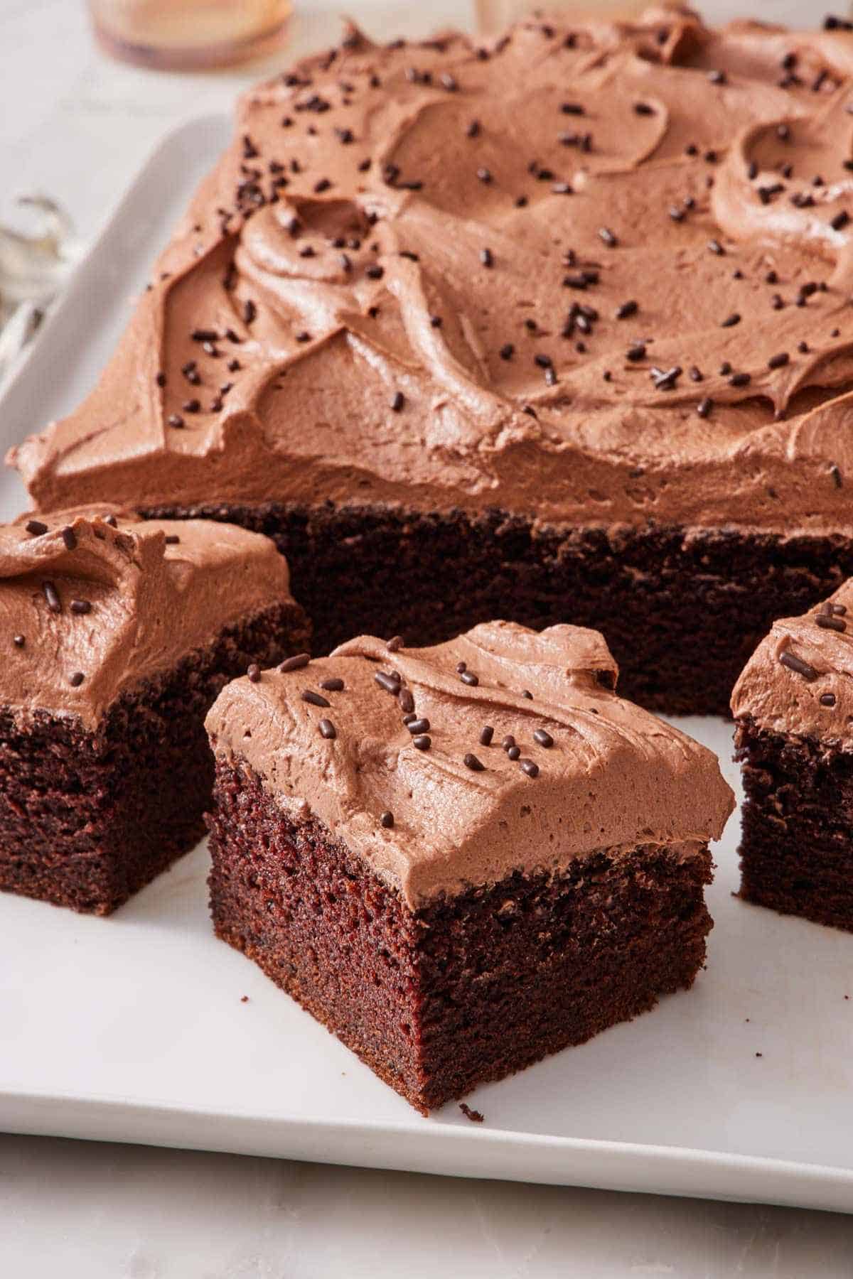 A few slices of chocolate sheet cake next to the rest of the unsliced cake.