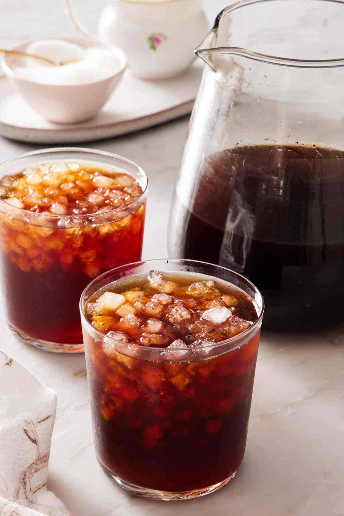 Two glasses of cold brew next to a pitcher with more coffee.