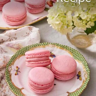 Pinterest graphic showing a few French macarons on a plate next to a vase of flowers. More macarons on a platter in the background.