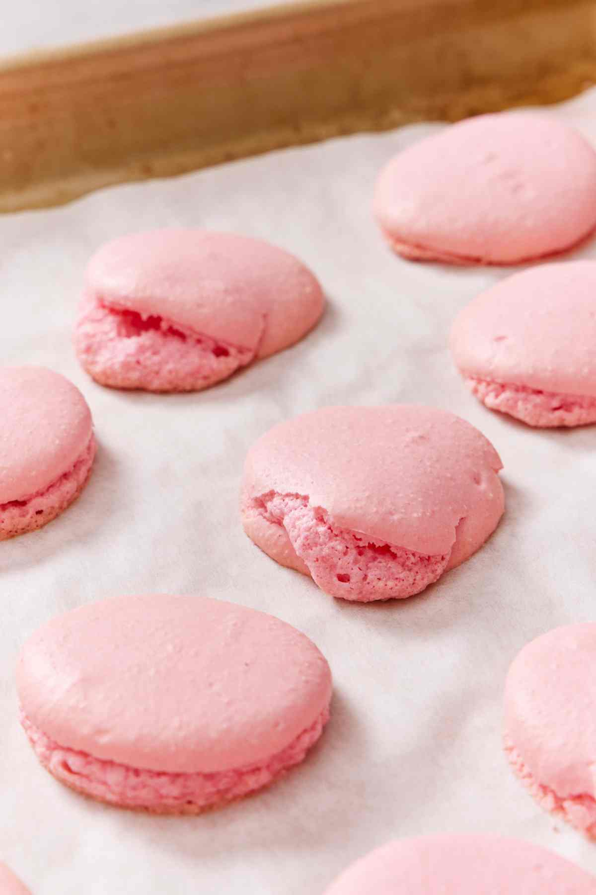 Several macaron recipe shells that baked slanted on a baking tray.