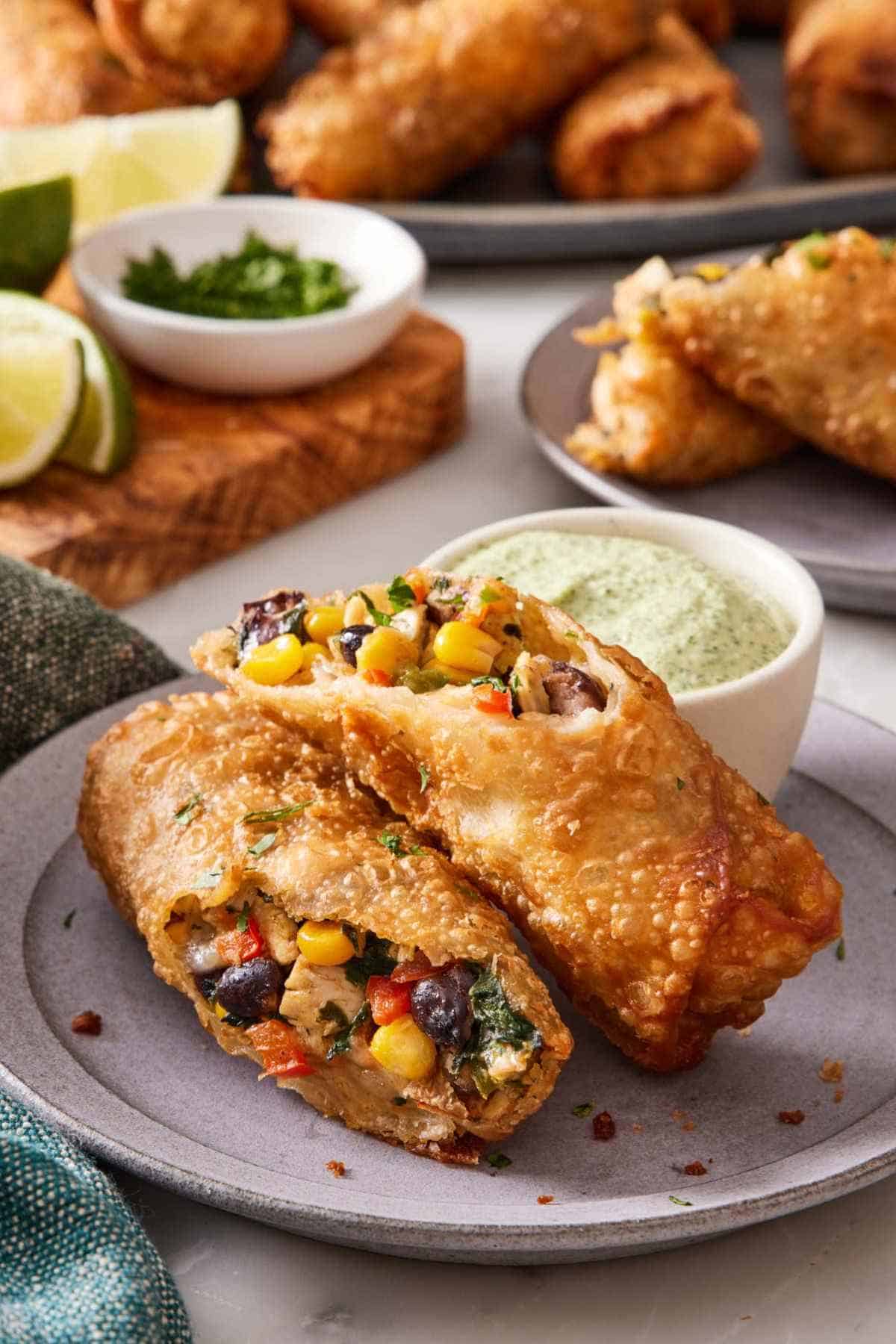 A southwest egg roll broken in half and set on a plate with a small ramekin of dippig sauce.