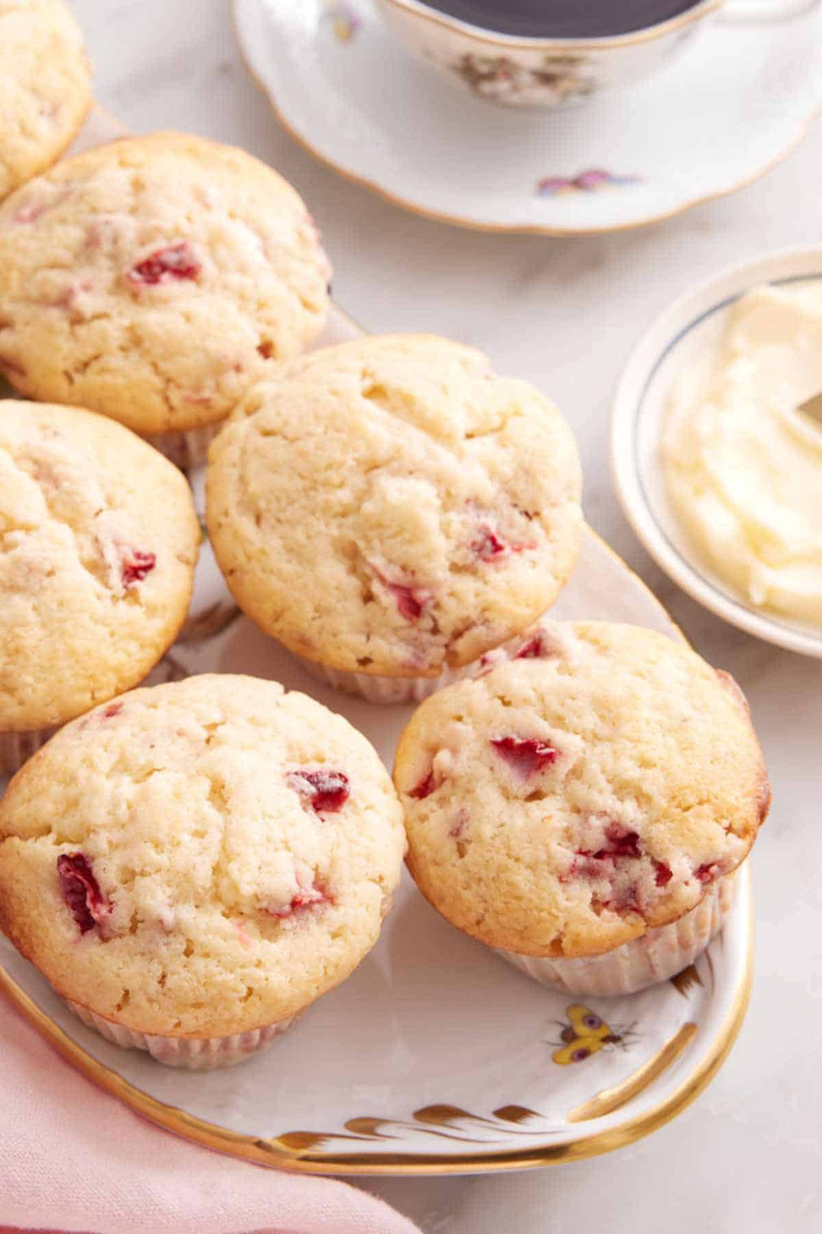 A platter of strawberry muffins, with butter and a cup of coffee mostly out of frame.