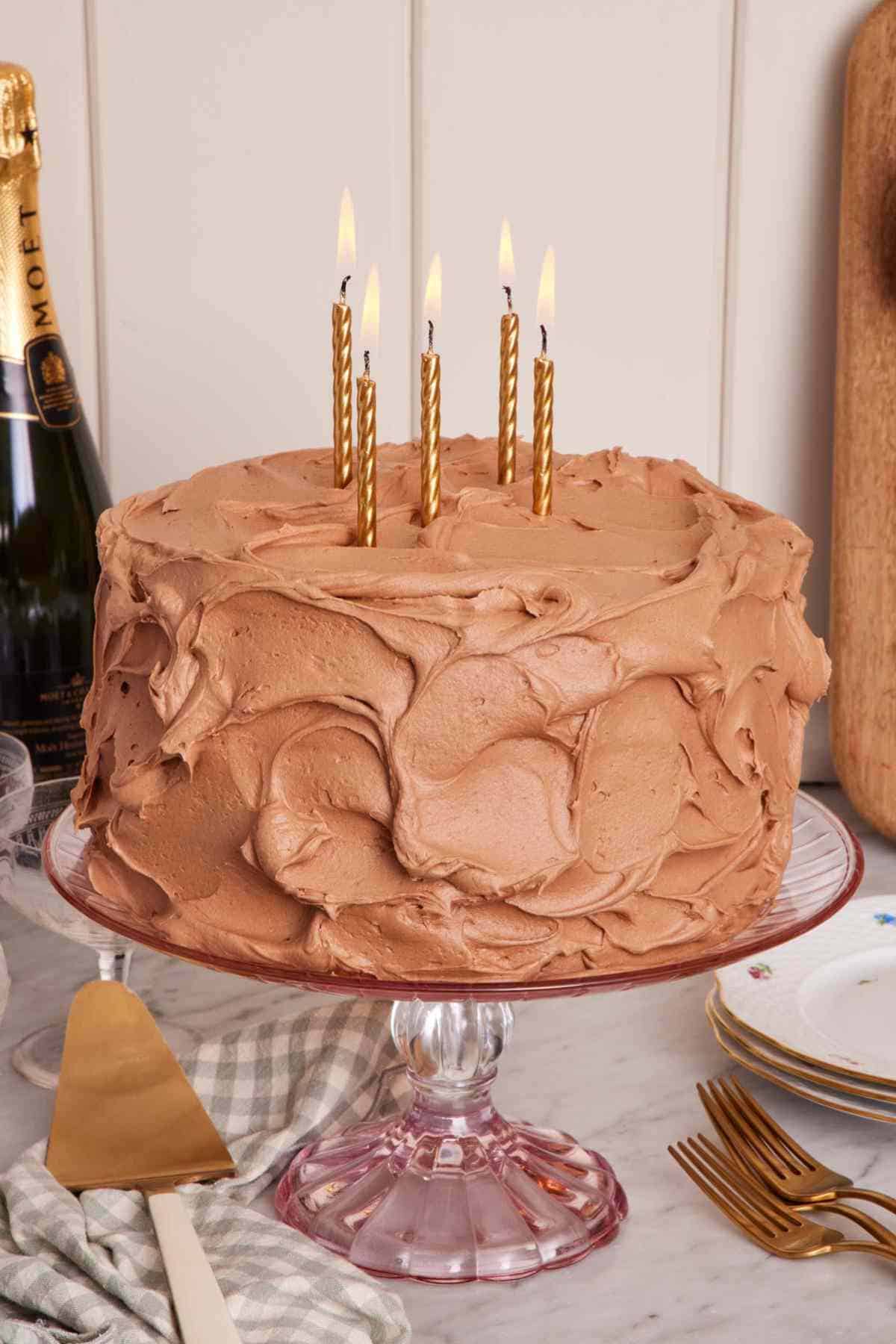 Frosted yellow cake on a cake stand with candles in it.