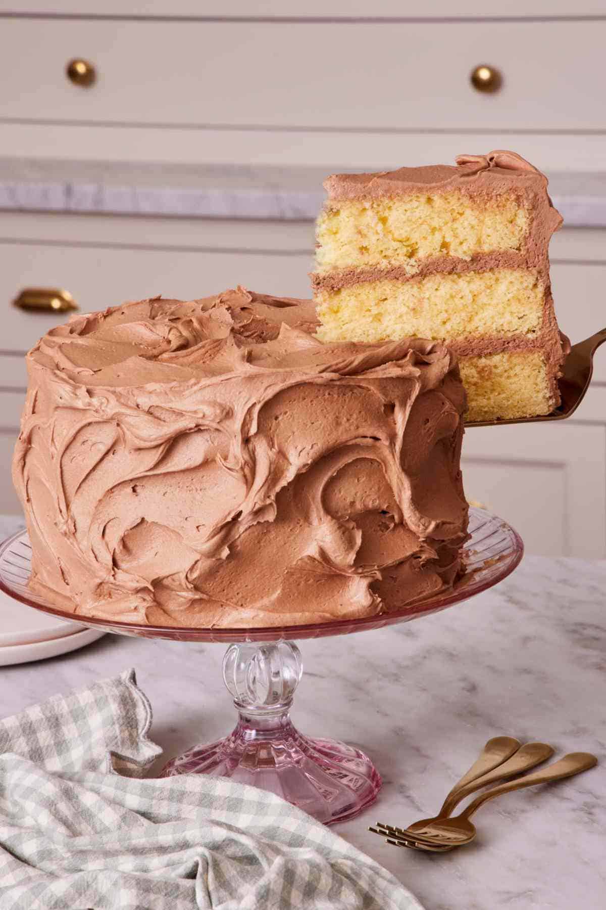 Yellow cake on a cake stand with a slice being lifted off.