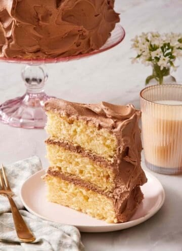 A slice of yellow cake standing up on a small plate alongside a glass of milk.