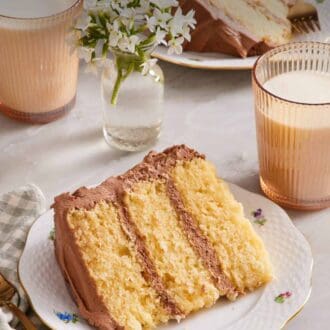 Pinterest graphic showing a slice of yellow cake laying down on a small plate, with glasses of milk and a vase of flowers also in frame.
