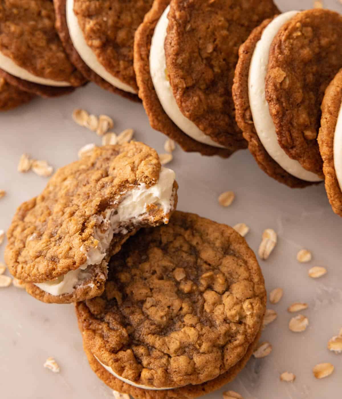 One oatmeal cream pie with a bite taken out leaning against another, with a row of oatmeal creme pies next to it.